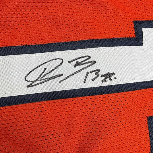 Close-up of autographed white stripe on orange Denver Broncos football jersey showing handwritten signature and number.