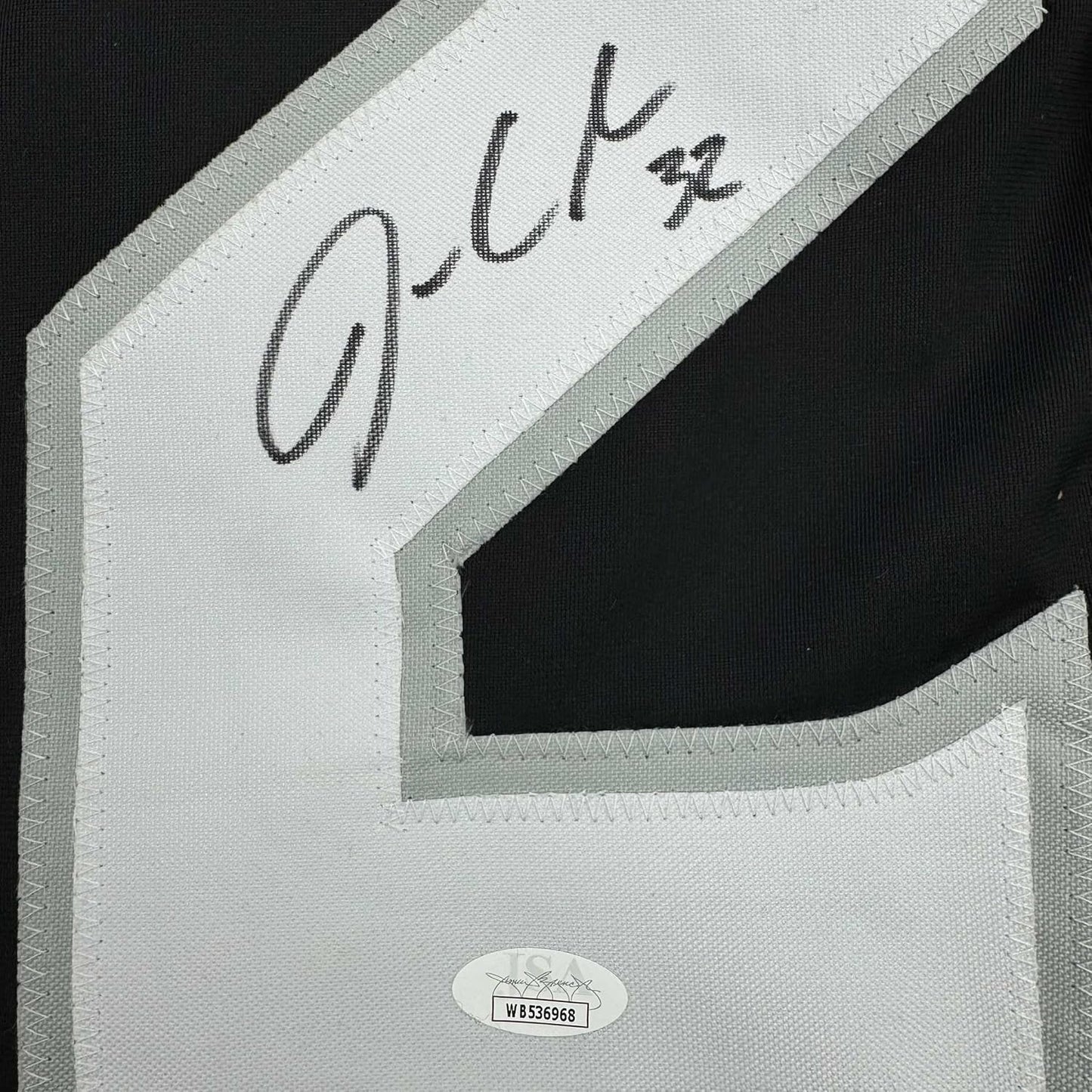 Close-up of handwritten signature on white fabric label with JSA authentication sticker visible below.