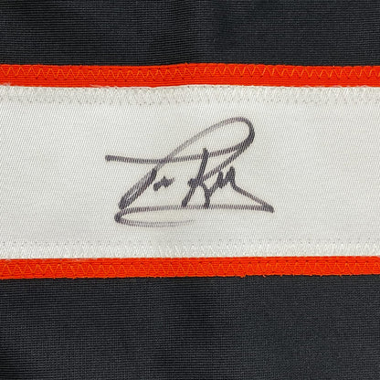 Close-up of embroidered signature on white jersey stripe between orange and black horizontal bands.