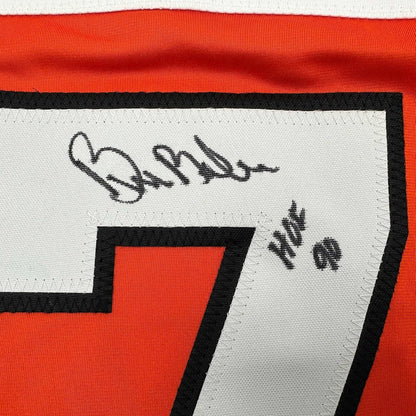 Close-up of autographed orange and black Philadelphia hockey jersey with signature and "HOF 90" printed on white panel.