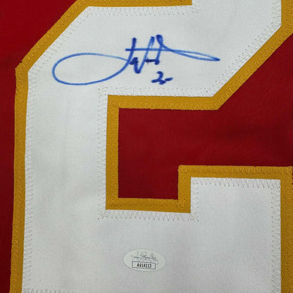 Close-up of blue autograph signature on white jersey panel with gold and red trim, JSA authentication sticker visible below.