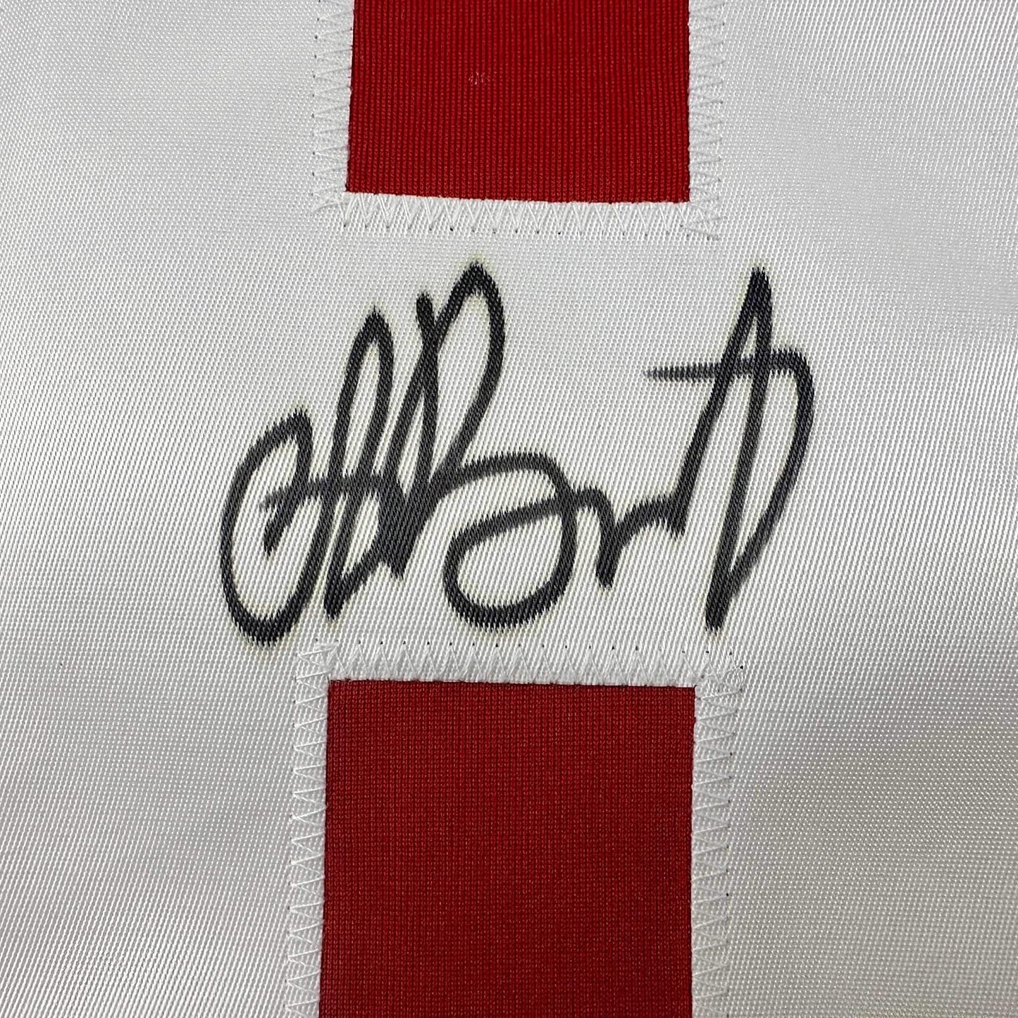 Close-up of handwritten black signature on white fabric between red ribbed trim sections of hockey jersey.