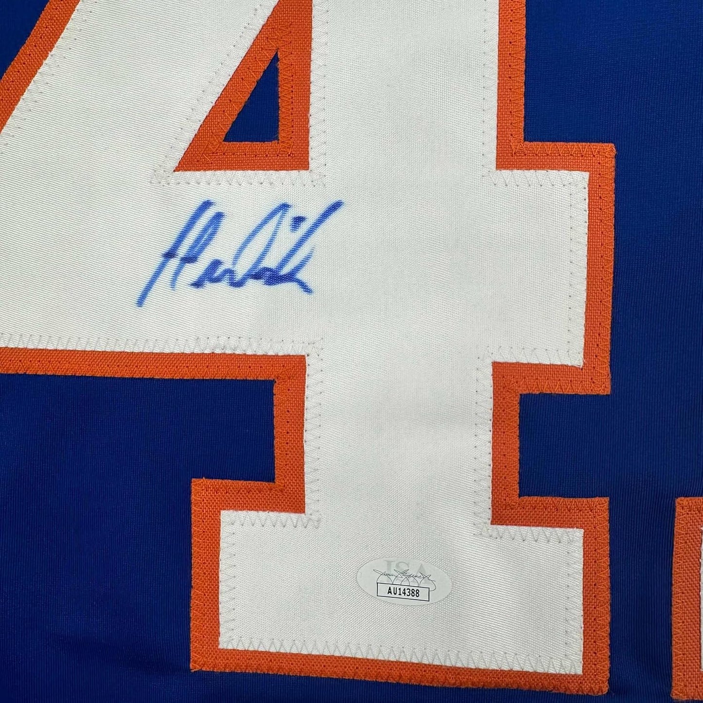 Close-up of blue autographed signature and JSA authentication sticker on white jersey panel with orange and blue trim.
