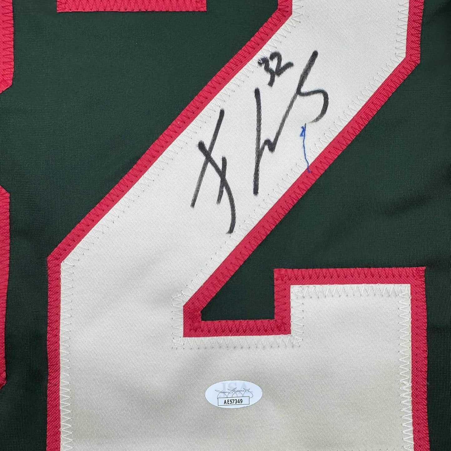 Close-up of signed green and red hockey jersey showing autographed white nameplate strip with JSA authentication sticker below.