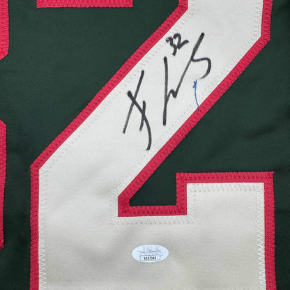 Close-up of signed green and red hockey jersey showing autographed white nameplate strip with JSA authentication sticker below.