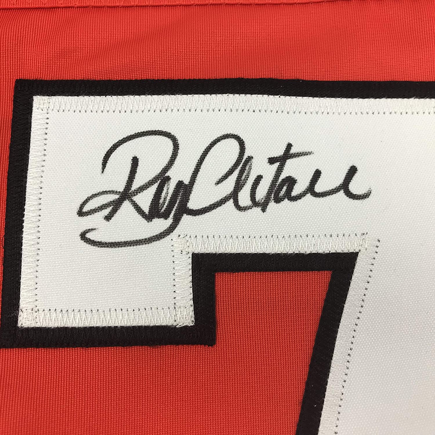 Close-up of white woven label with "Ron Hextall" signature in black cursive on red and black jersey fabric.
