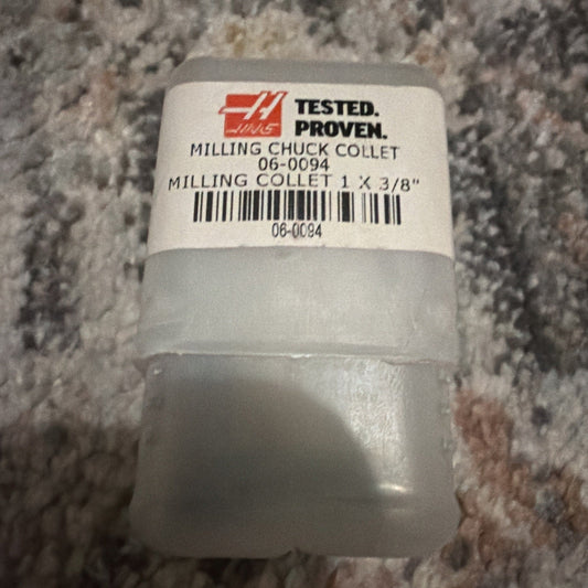 White cylindrical milling chuck collet with printed label showing "TESTED. PROVEN." logo and product details 06-0094, photographed from above on textured gray surface.