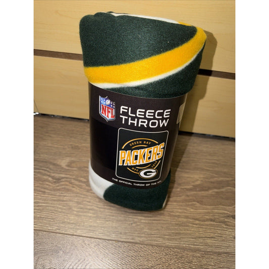 Green Bay Packers fleece throw blanket rolled and displayed on wooden floor showing dark green, yellow, and white colors with NFL branding label.
