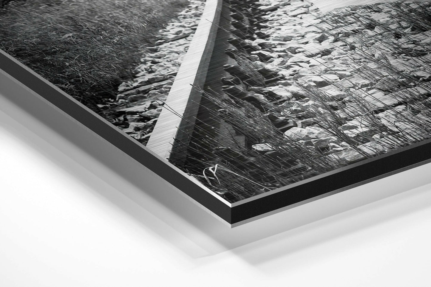 Angled perspective view of framed black and white photograph with brushed aluminum and black border mounted on white background.