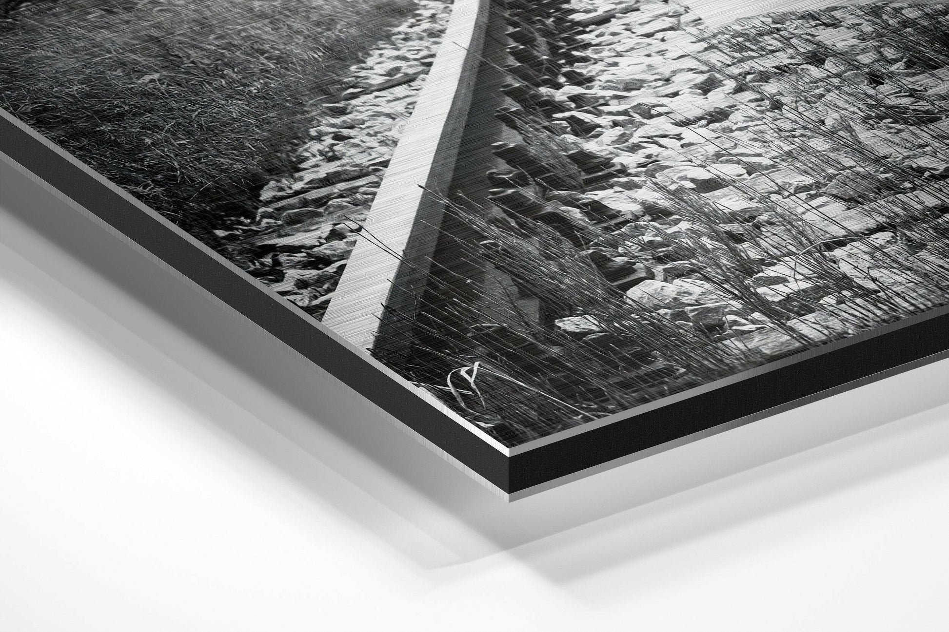 Angled perspective view of framed black and white photograph with brushed aluminum and black border mounted on white background.