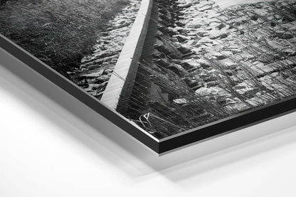 Angled perspective view of framed black and white photograph with brushed aluminum and black border mounted on white background.