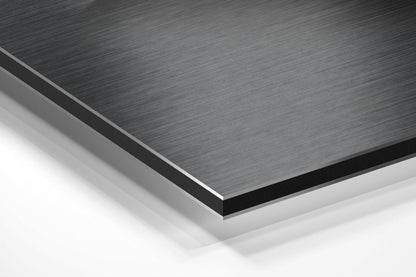 Close-up angled view of stacked Dibond panels showing brushed aluminum surface texture in gray and white layers.
