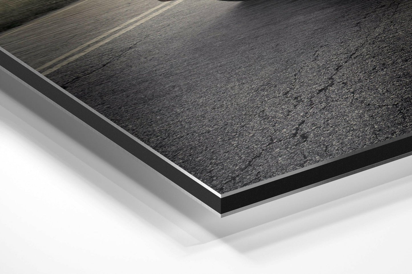 Close-up angled view of layered Dibond panel showing textured dark gray surface with white base layer and black edge trim.