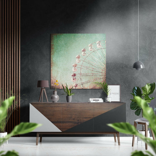 Ferris wheel wall art in pastel green and pink tones displayed above a wooden dresser in a modern interior setting with plants and decor.