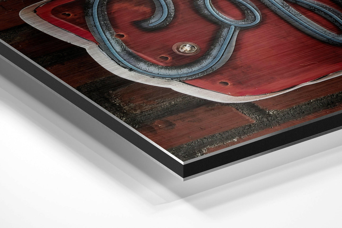 Close-up angled view of layered Dibond panel showing brushed aluminum and black border edges with red and dark wood-textured artwork surface.