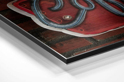 Close-up angled view of layered Dibond panel showing brushed aluminum and black border edges with red and dark wood-textured artwork surface.