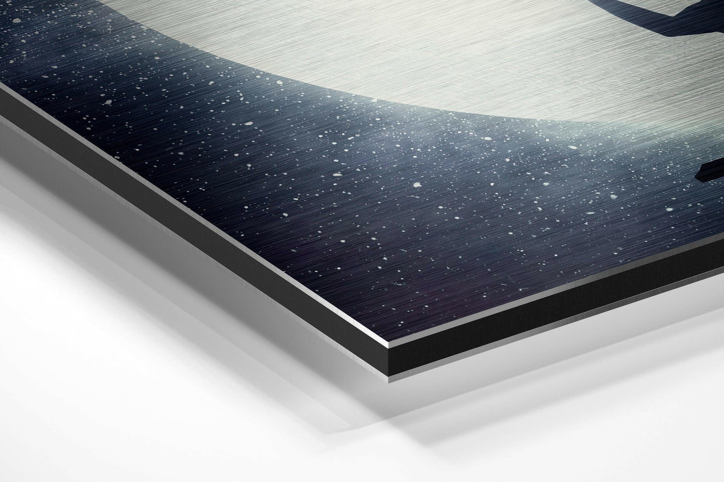 Close-up angled view of layered Dibond wall art showing dark brushed aluminum surface with white speckles and light wood grain panel above, displaying edge construction and material depth.