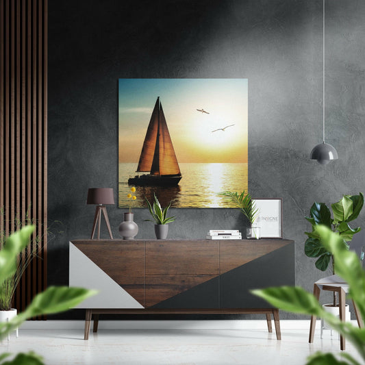 Sailboat at golden sunset displayed above wooden dresser in modern interior with gray textured wall and potted plants.