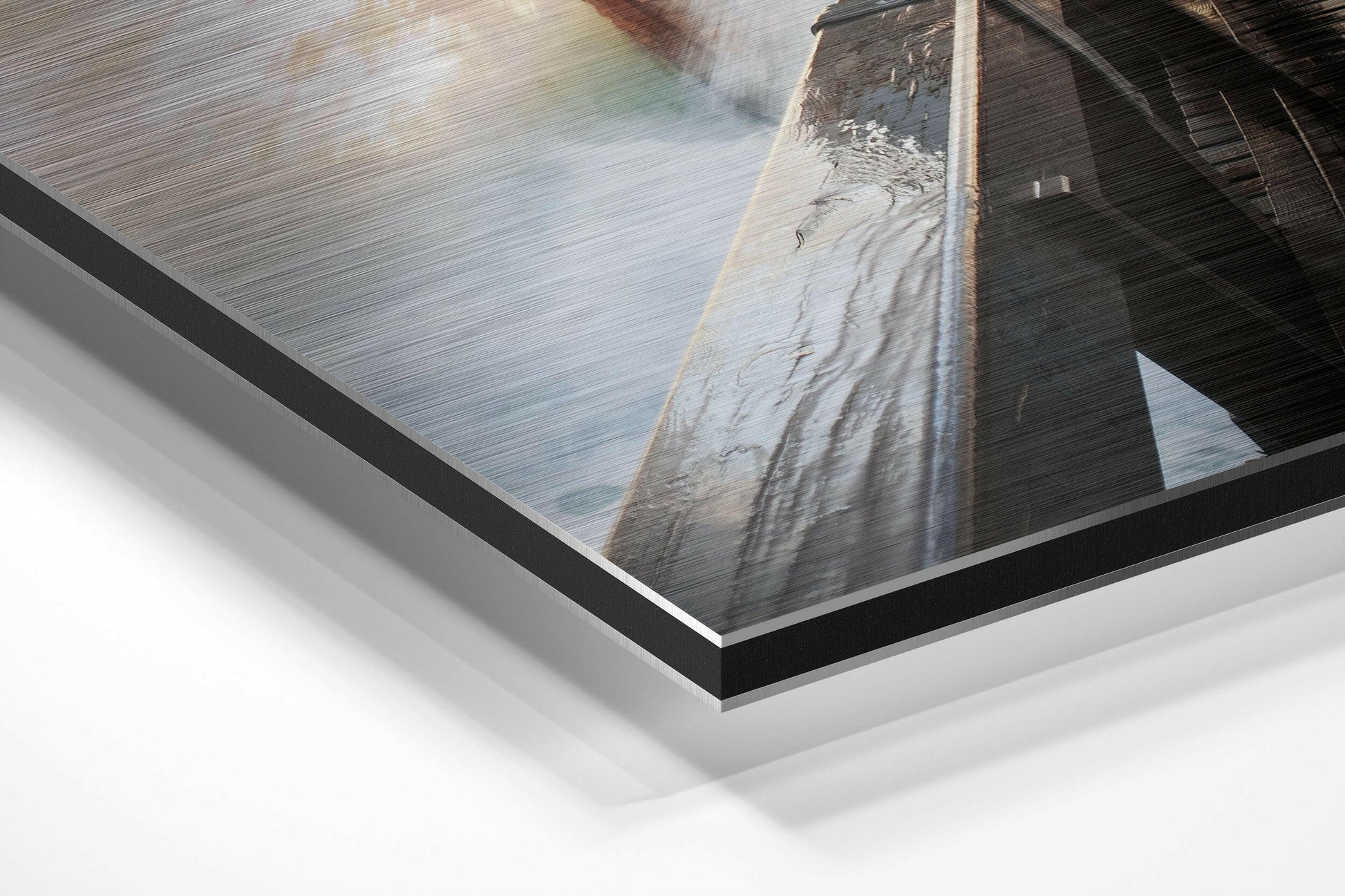 Close-up angle view of brushed aluminium Dibond print showing layered frame edge with lighthouse and water photograph visible through transparent layers.