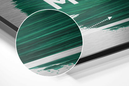 Close-up angled view of brushed aluminium wall art with green and white striped pattern and circular magnified detail.