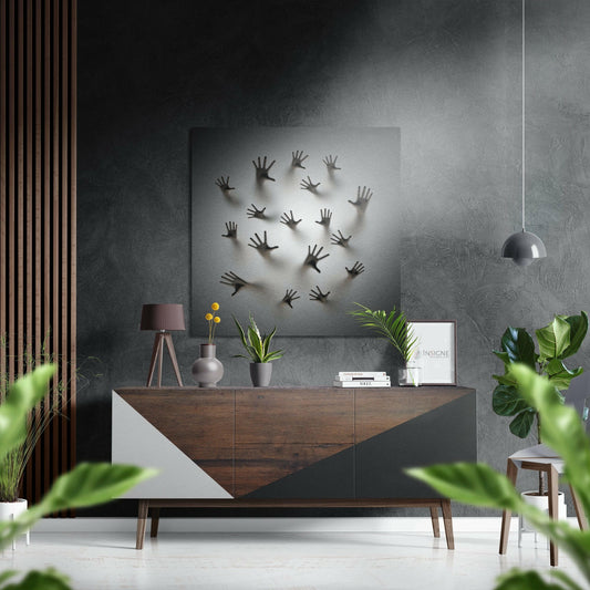 Brushed aluminum wall art featuring multiple raised hand silhouettes displayed above a wooden dresser in a modern interior setting.