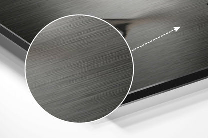 Close-up angled view of brushed aluminum Dibond sheet showing circular cutout detail with directional arrow on textured metallic surface.