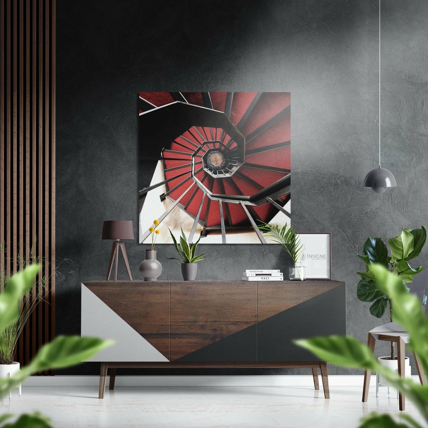 Red spiral staircase Dibond art displayed above wooden console table in modern grey interior with plants and pendant light.