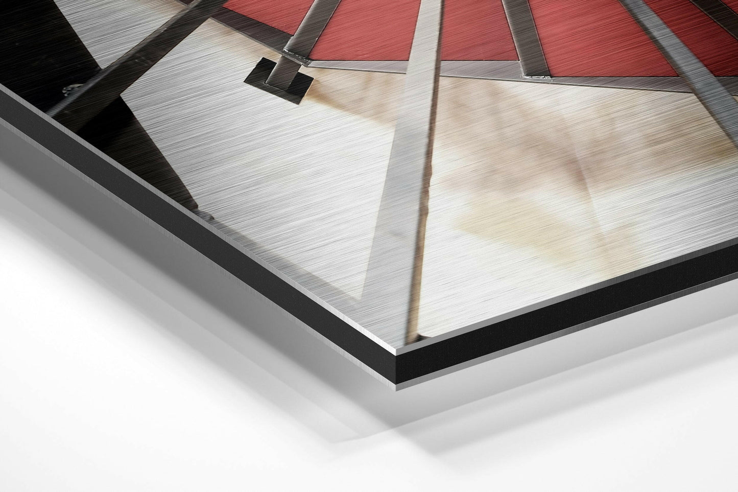 Angled close-up of framed Dibond wall art showing brushed aluminum surface with red and white geometric design and black border.