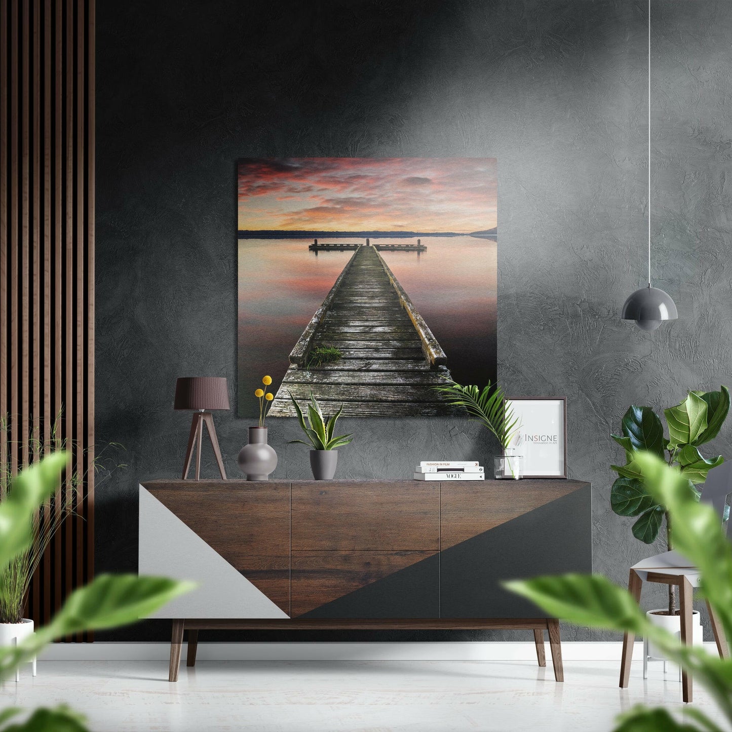 Wooden pier extending into calm water at sunset, displayed as metal wall art above a mid-century modern dresser in a styled interior.
