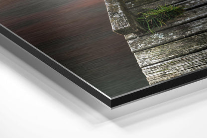 Close-up angled view of brushed aluminum Dibond print showing layered edges and weathered wooden dock with water reflection.