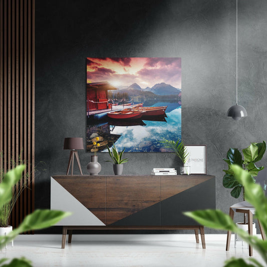 Brushed aluminium Dibond wall art depicting red boats on turquoise water at sunset with mountains, displayed above wooden dresser in modern interior.