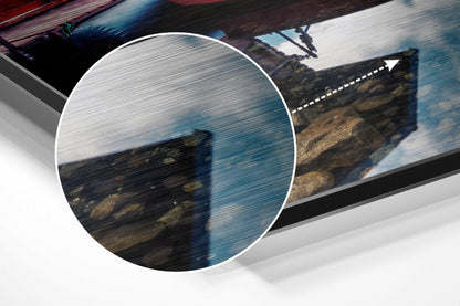 Brushed aluminium Dibond wall art displaying a coastal seascape with rocky cliffs and blue water, shown at an angled perspective.