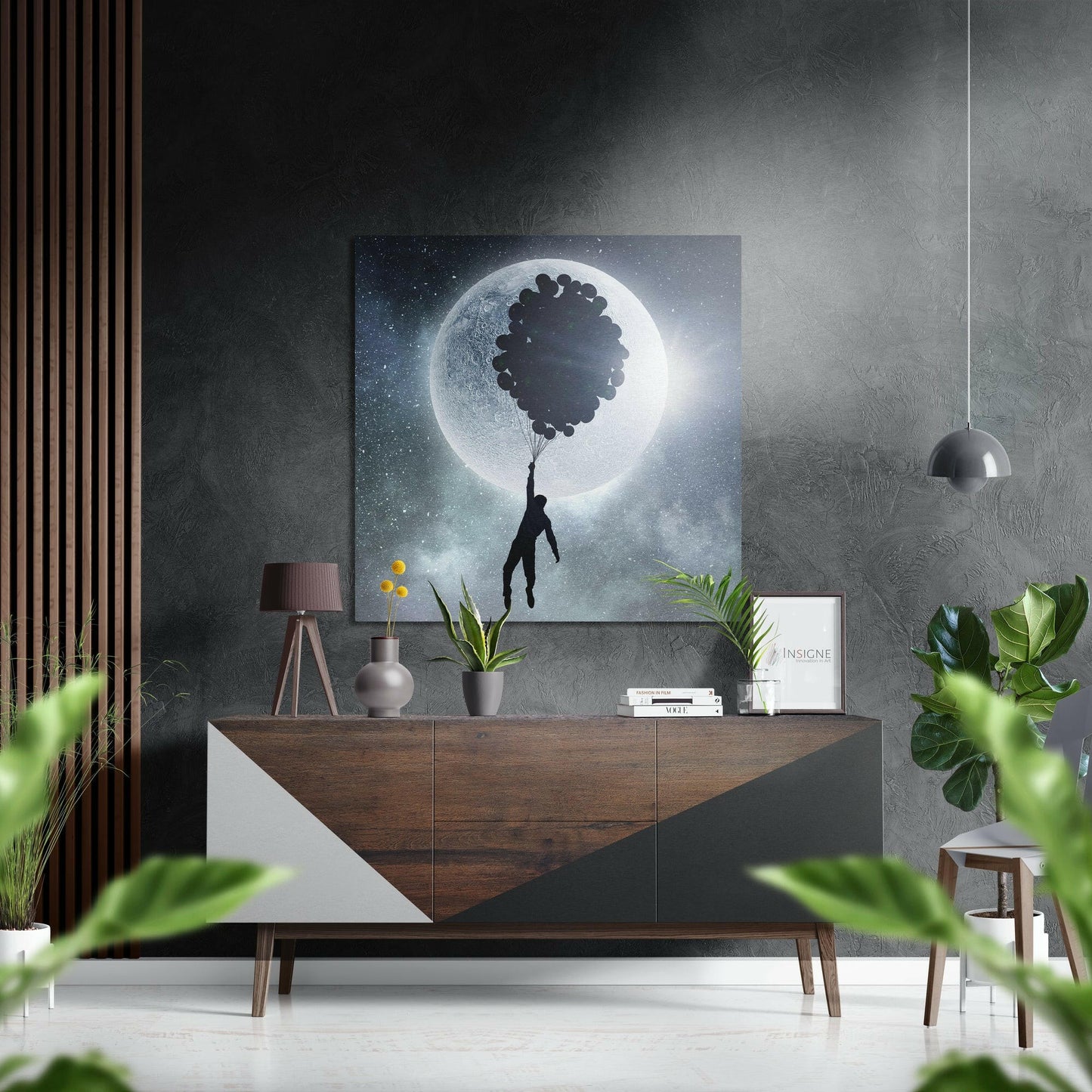 Surreal artwork featuring silhouetted figure holding balloons against glowing moon in starry night sky, displayed above wooden dresser in modern interior.