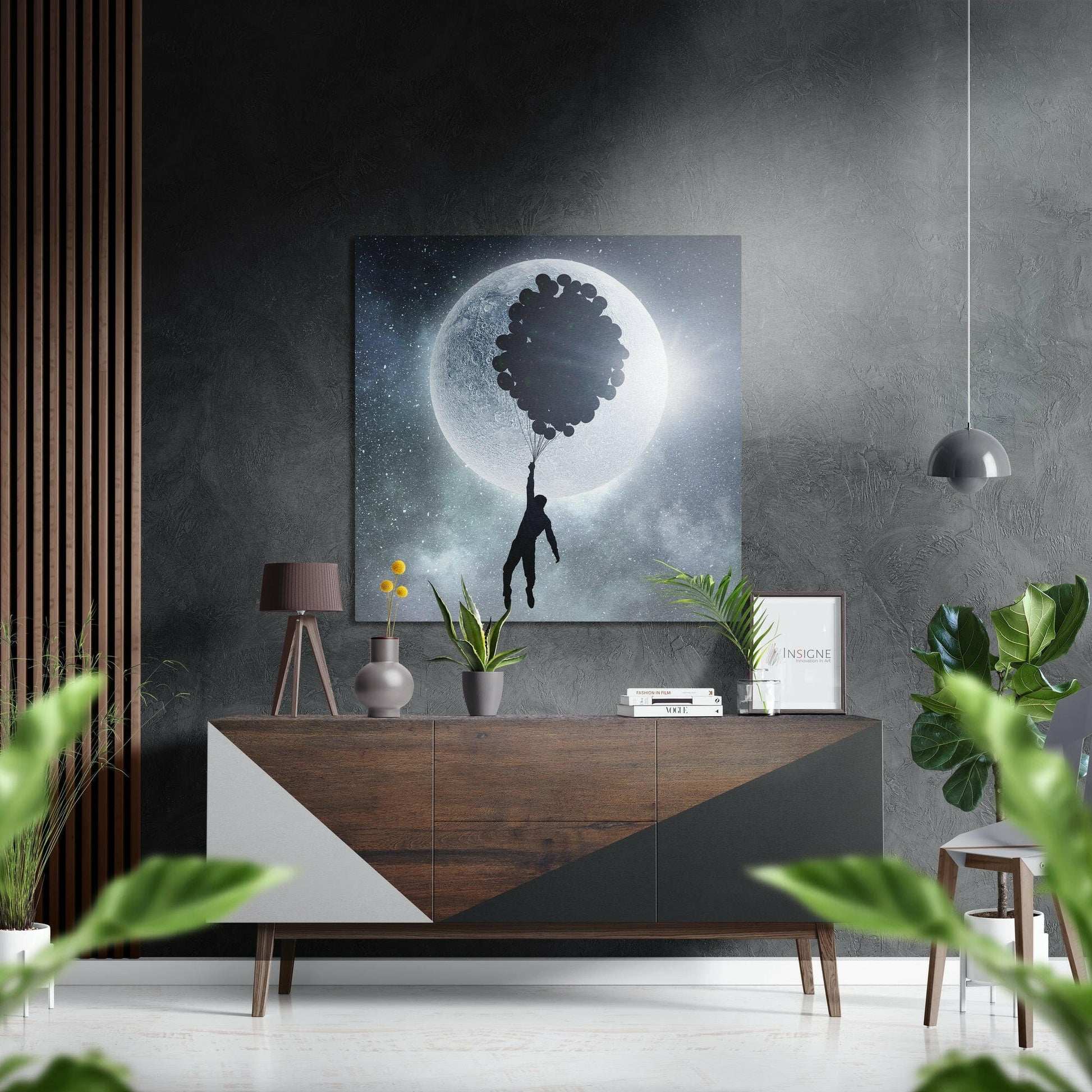 Surreal artwork featuring silhouetted figure holding balloons against glowing moon in starry night sky, displayed above wooden dresser in modern interior.