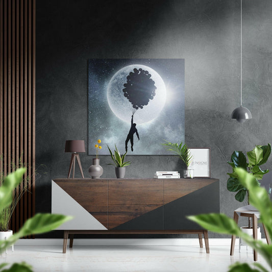 Surreal artwork featuring silhouetted figure holding balloons against glowing moon in starry night sky, displayed above wooden dresser in modern interior.