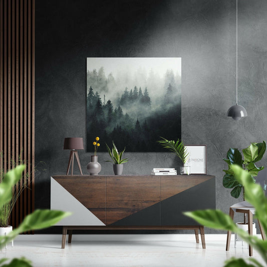 Foggy forest wall art displayed above a wooden dresser in a modern interior with plants and pendant lamp.