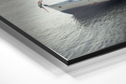 Angled view of brushed aluminum Dibond print showing a parrot perched on a wooden boat dock with calm water, with layered mounting and shadow visible.