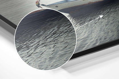 Close-up detail of brushed aluminum surface showing linear texture and grain patterns with water reflections and wooden dock in background.