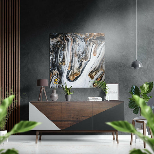Black, white, and gold marbled abstract artwork displayed on dark textured wall above wooden dresser with styling accessories.