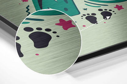 Angled close-up of brushed aluminium wall art showing magnified paw print design with dark navy paws, pink accents, teal leaf shapes, and textured surface.