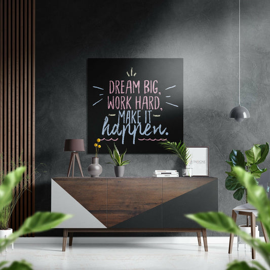 Motivational quote wall art displaying "Dream Big, Work Hard, Make It Happen" in pastel chalk lettering on black background, mounted above wooden dresser in modern interior setting.