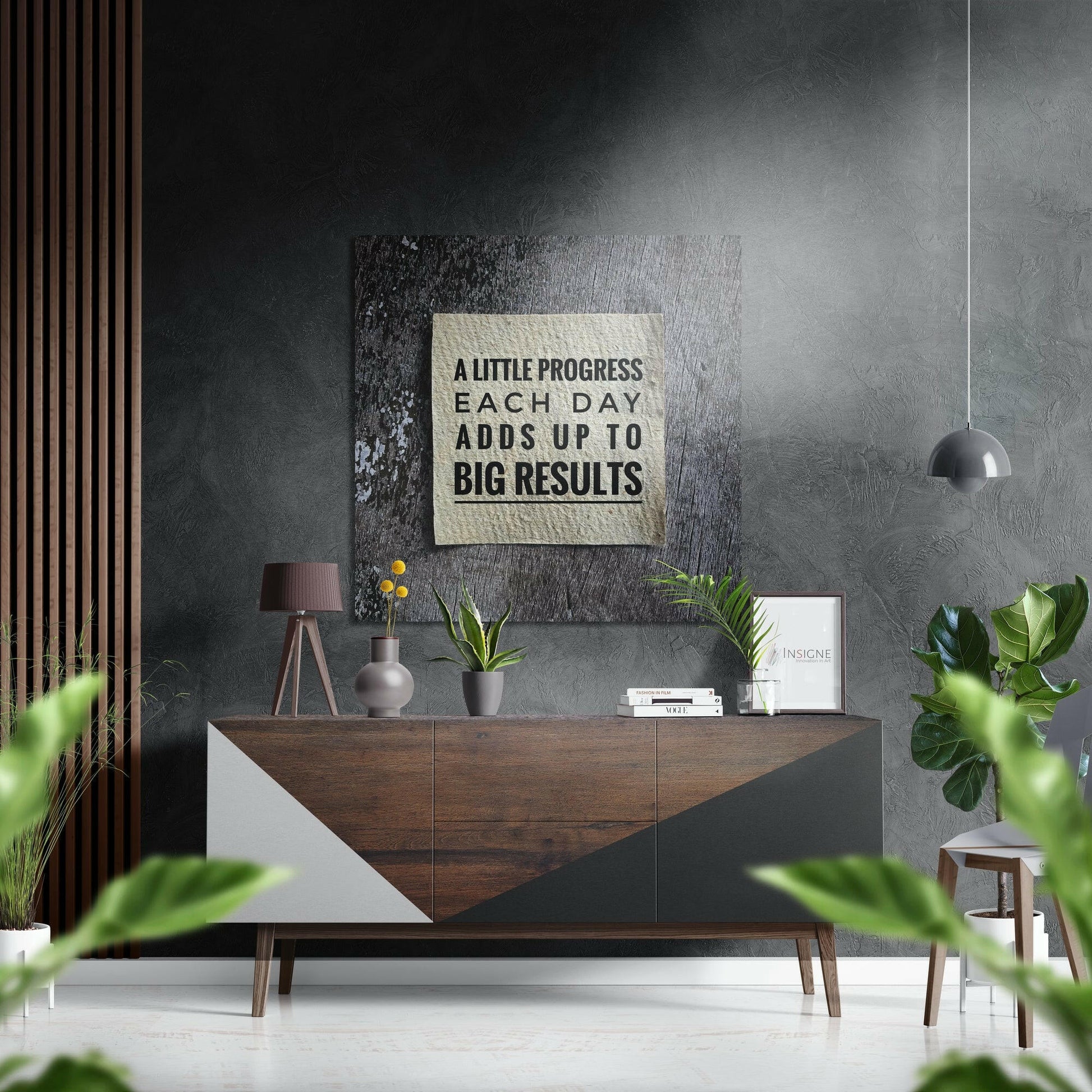 Motivational brushed aluminium wall art with black text "A LITTLE PROGRESS EACH DAY ADDS UP TO BIG RESULTS" mounted above a mid-century wooden dresser in a modern interior.
