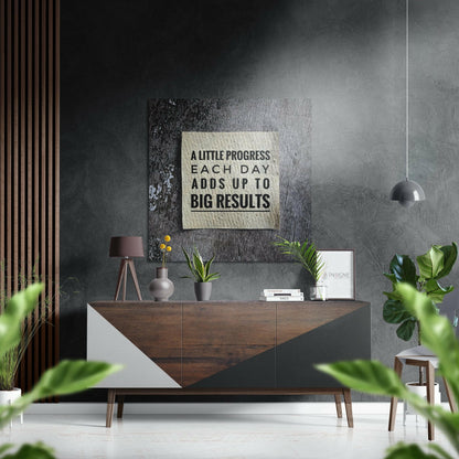Motivational brushed aluminium wall art with black text "A LITTLE PROGRESS EACH DAY ADDS UP TO BIG RESULTS" mounted above a mid-century wooden dresser in a modern interior.