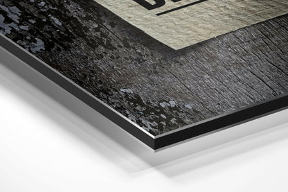 Close-up angled view of layered Dibond wall art showing black brushed aluminum surface with light gray and cream-colored geometric sections above.
