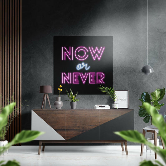 Modern interior styled with neon "NOW or NEVER" sign in pink and blue mounted above wooden dresser with plants and accessories.