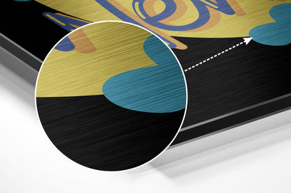 Close-up angled view of brushed aluminum wall art showing yellow, teal, and black abstract design with white circular magnification detail.