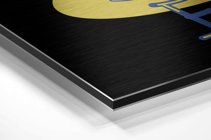 Close-up angled view of layered Dibond panel showing black brushed aluminum surface with white backing and yellow logo detail at top.