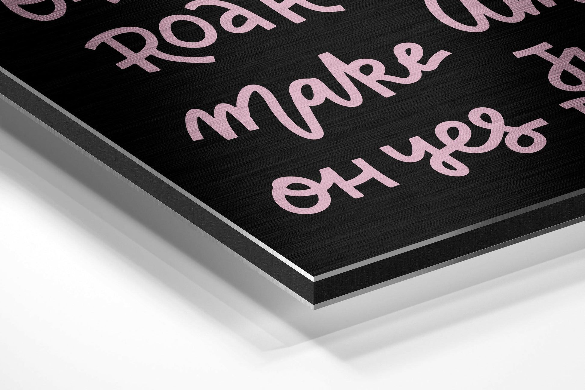 Close-up angled view of brushed black aluminum dibond panel with pink metallic text and layered edge detail against white background.