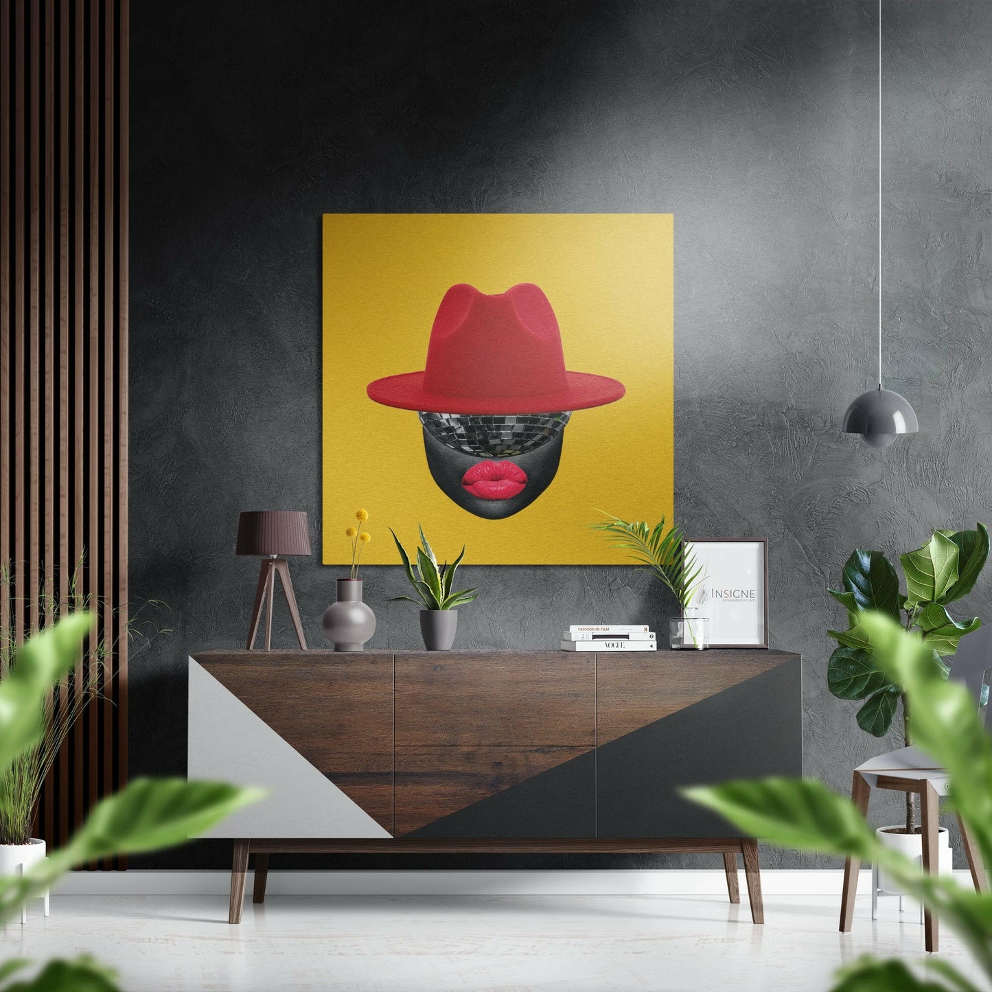 Bold yellow square wall art featuring stylized portrait with red hat, disco ball face, and red lips displayed above mid-century wooden console in modern interior.