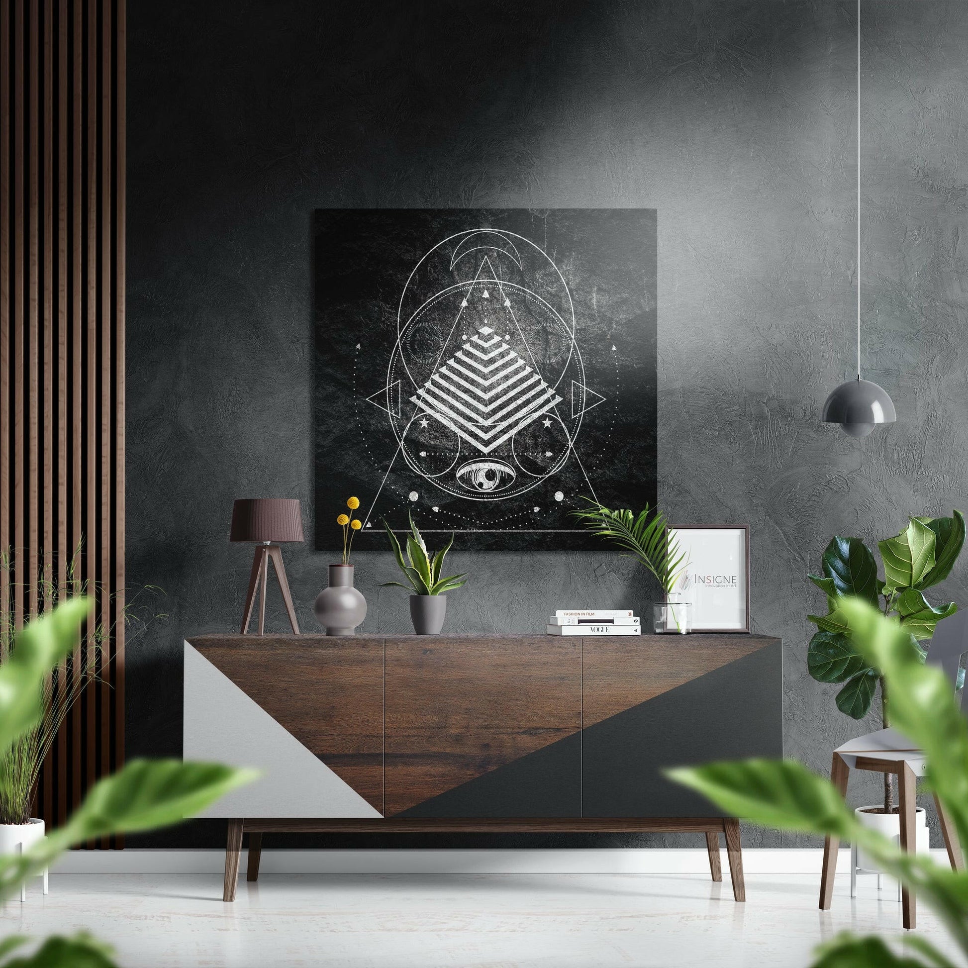 Modern interior styled shot showing geometric sacred art print hung above wooden console table with plants and decor in monochrome room.